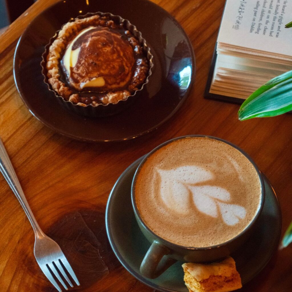 Honey Nut Latte with a baked mini scone on a wooden table with an open book in the corner
