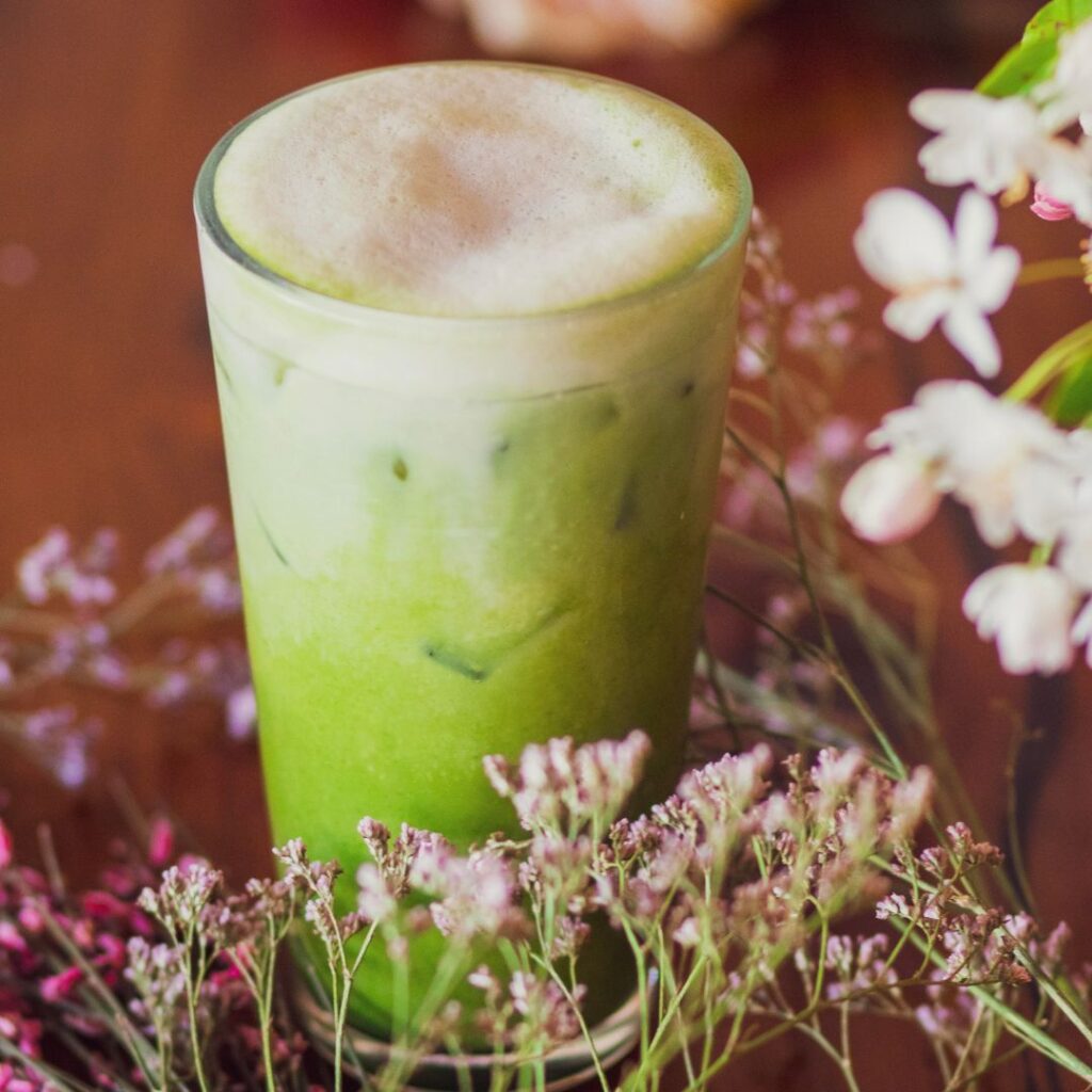 matcha latte in a glass cup with foam, surrounded by wild flowers on a wooden table