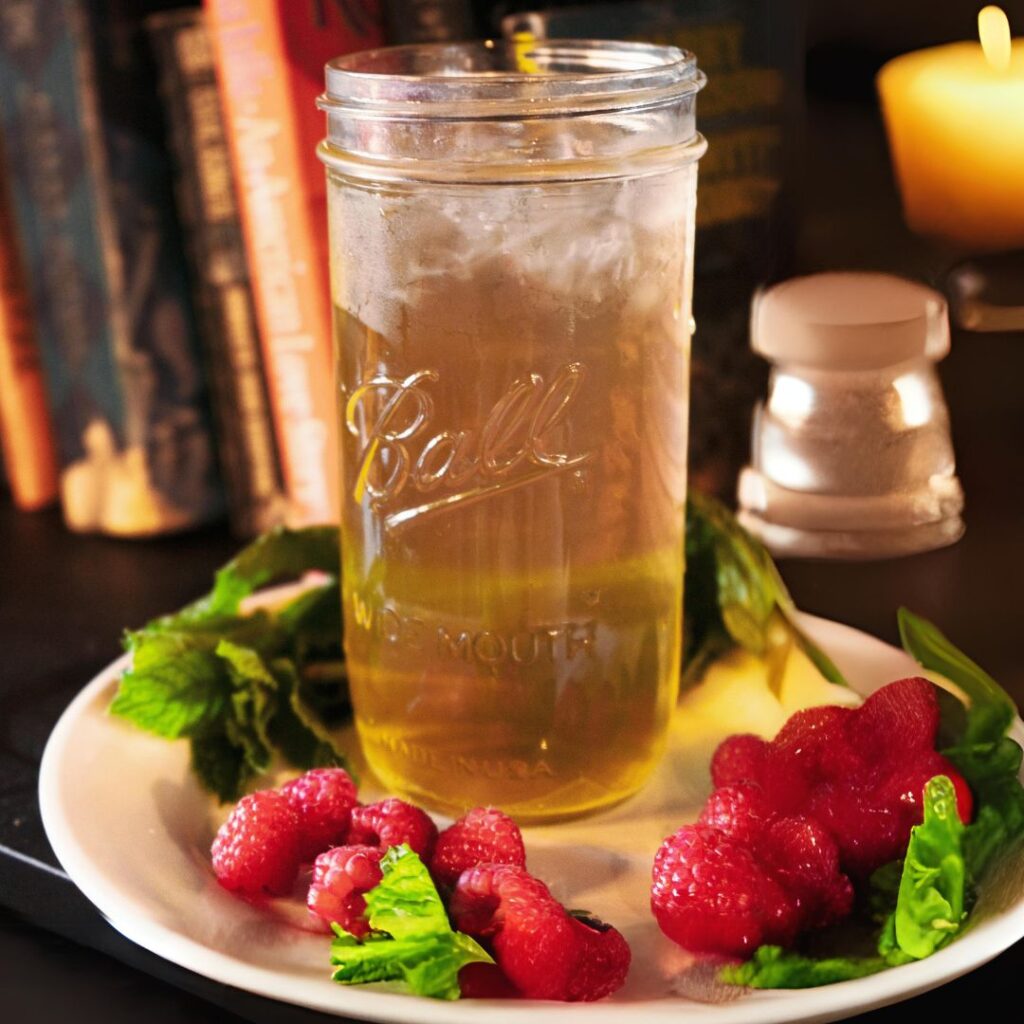 tall mason jar with tea on a plate surrounded by raspberries